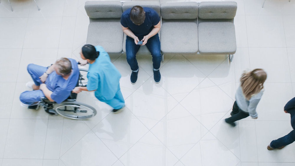 Overhead shot of Medical waiting room, including two women walking, doctor pushing man in wheelchair, and patient texting
