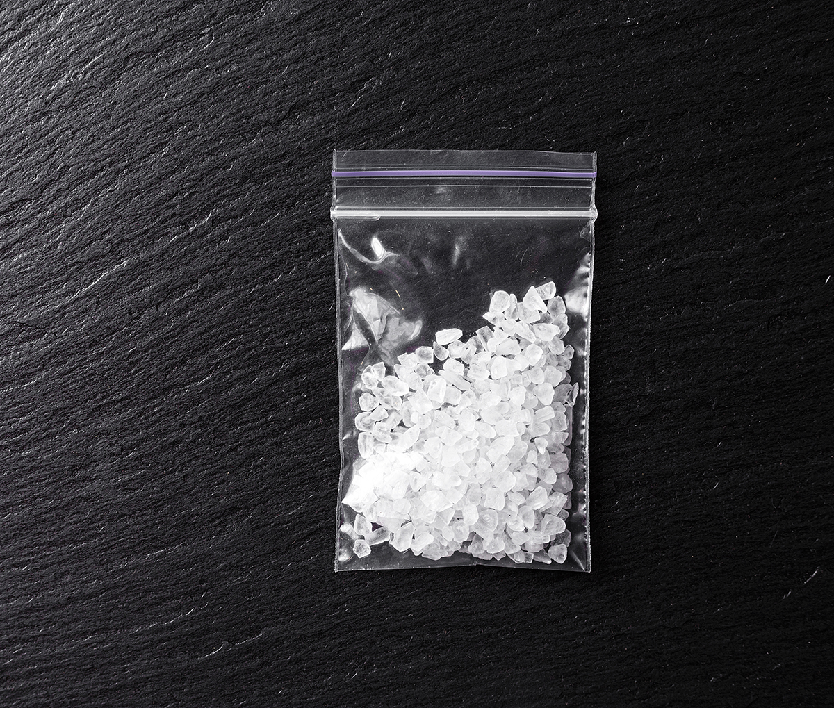 drugs in the form of crystals on a black background, methamphetamine in a plastic bag