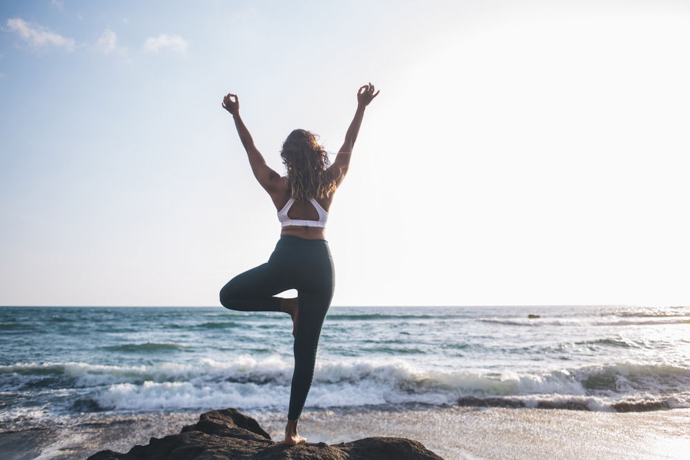 Rear view of woman doing yoga tree pose with raised arms and hands in lotus position