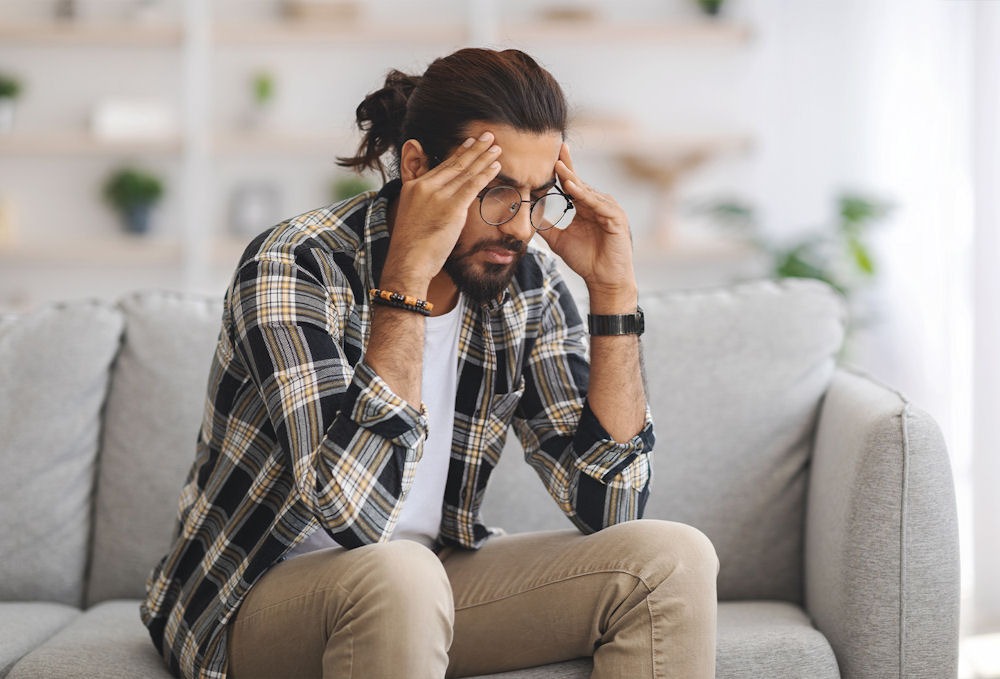 Man in glasses and flannel shirt rubbing temples while sitting