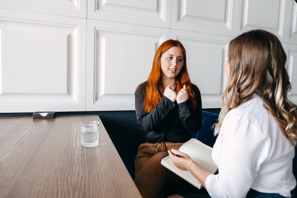 Woman with red hair opening up to therapist with both seated at table with full water glass