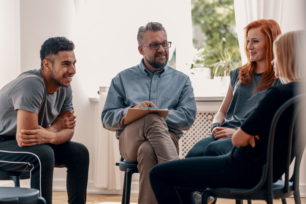 Mixed-gender addiction recovery group talking with older counselor