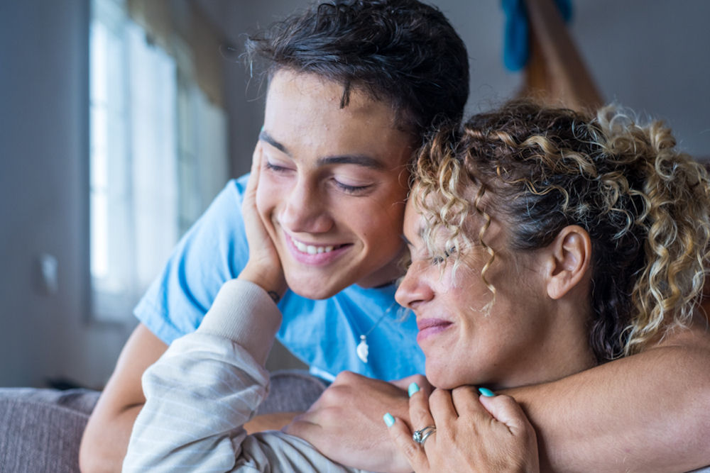 Seated woman reaching back to embrace son leaning over to embrace her