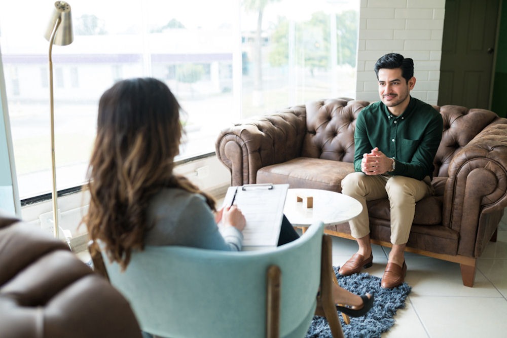 Man receiving therapy in comfortable office from therapist with partial blonde highlights