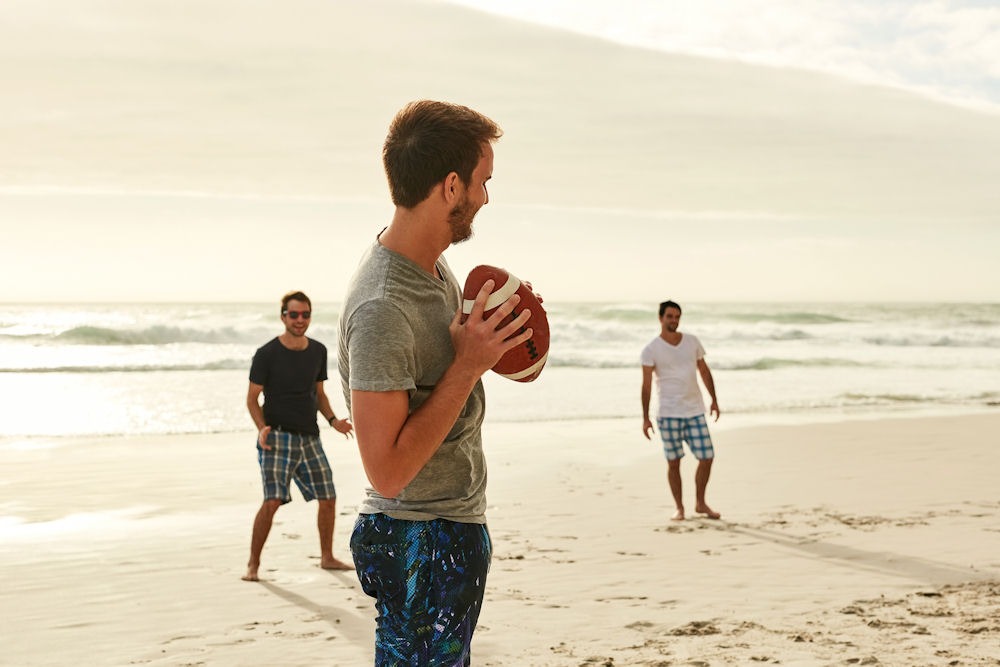 Three men playing football on the beach