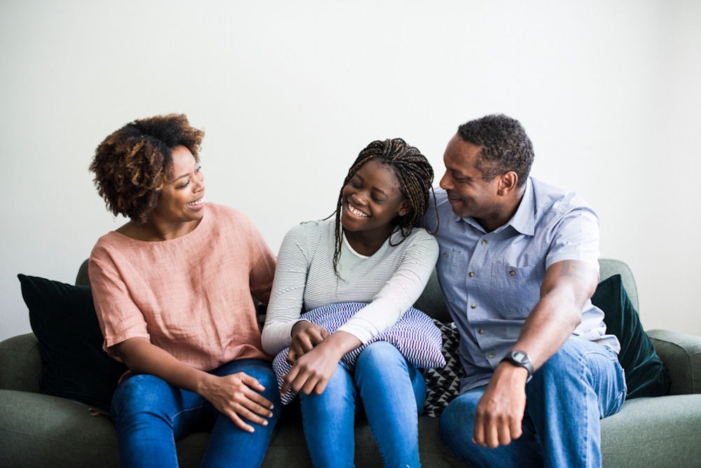 Family of mother, father, and daughter embracing and smiling on green couch