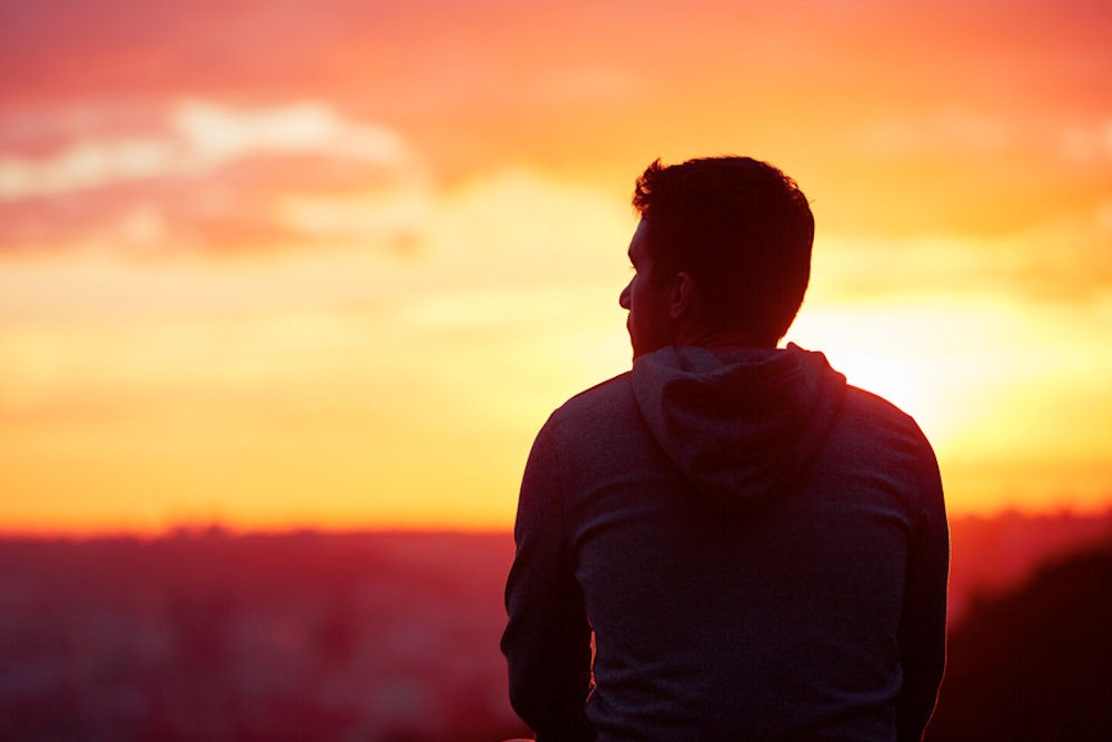 Rear view of man in grey hoodie watching the sun set over high desert