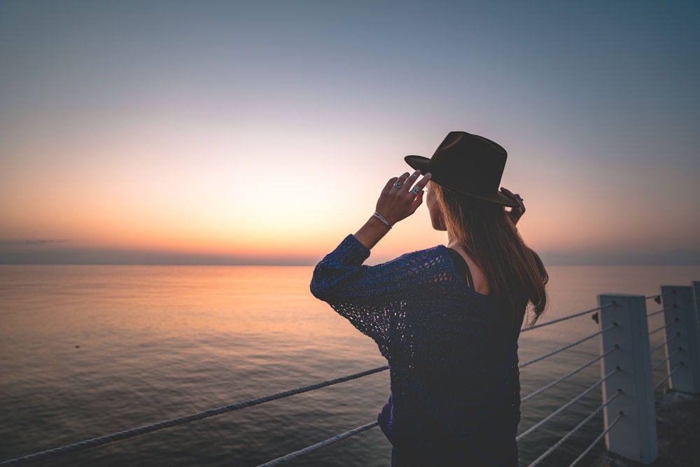 Woman in woven caftan looking out at ocean from dock