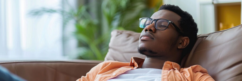 Man with glasses relaxing in an armchair, thinking about early sobriety