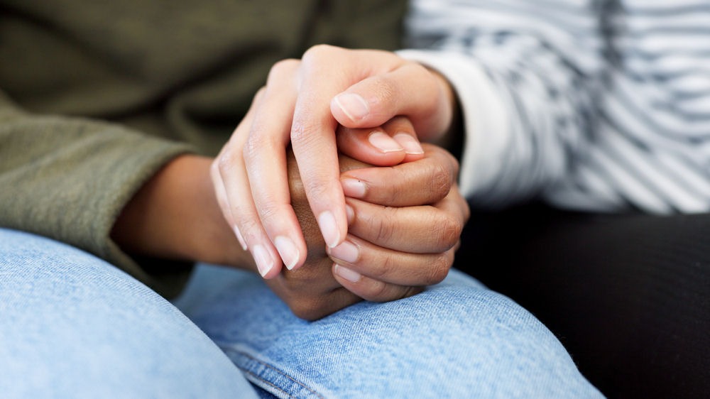 Close shot of friends clasping hands while discussing sobriety motivation.