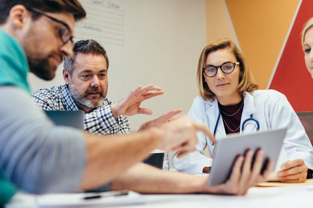 Doctor looking at iPad held up by startup founder and ideating advisor