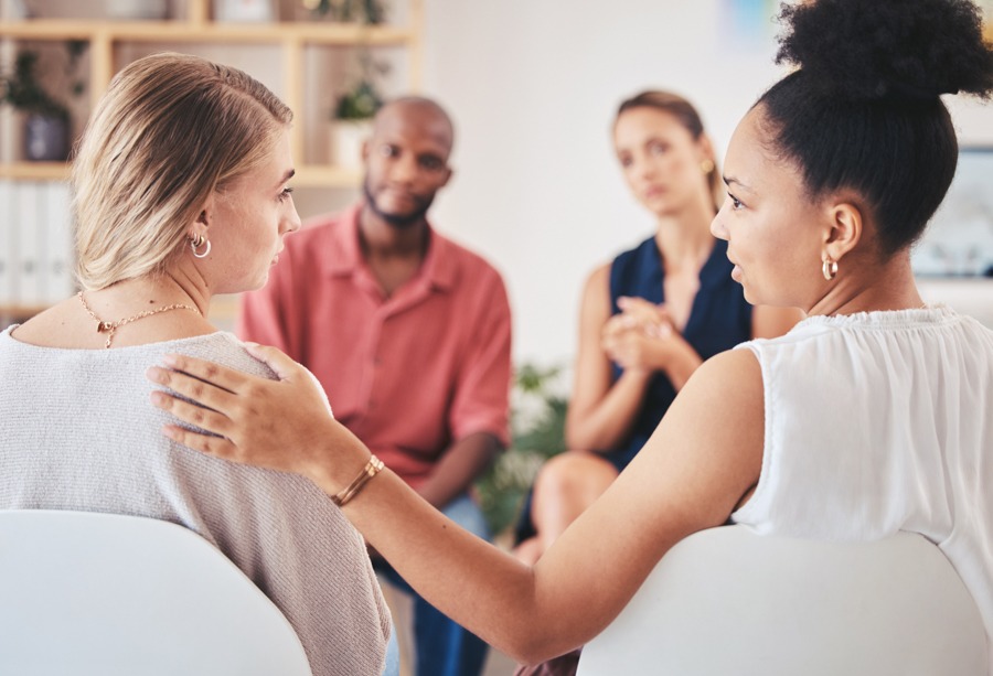 Woman reassuring another woman with a shoulder touch in an addiction support group