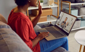 Woman saying hello to counselor visible on a laptop during online rehab program