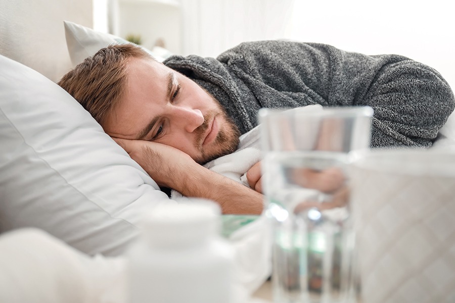 Depressed man in bed across with glass of water and pain medication on nightstand