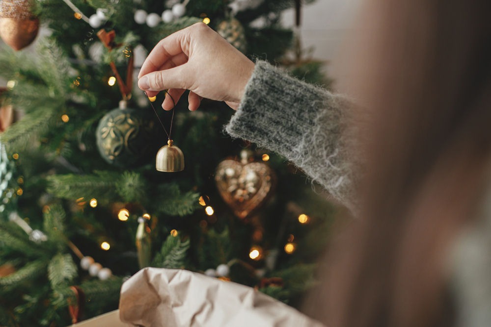 Over-the-shoulder picture of a woman hanging up Christmas ornaments on a pine tree with lights