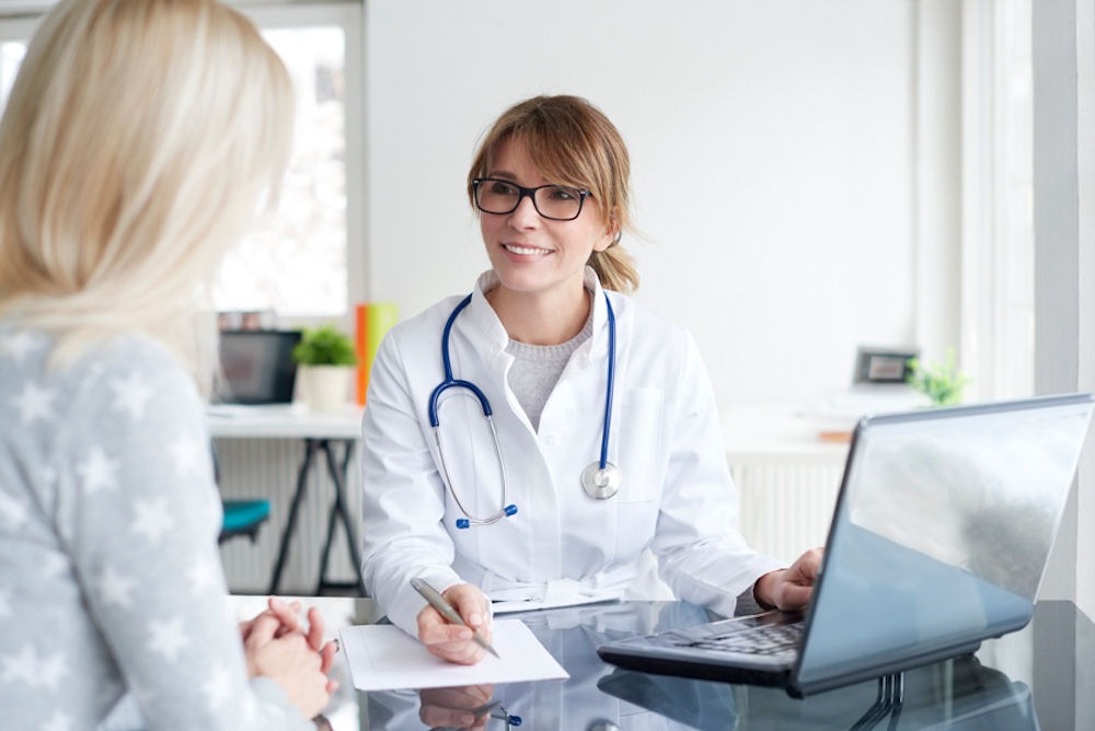 Doctor with stethoscope and laptop explaining online rehab program to patient