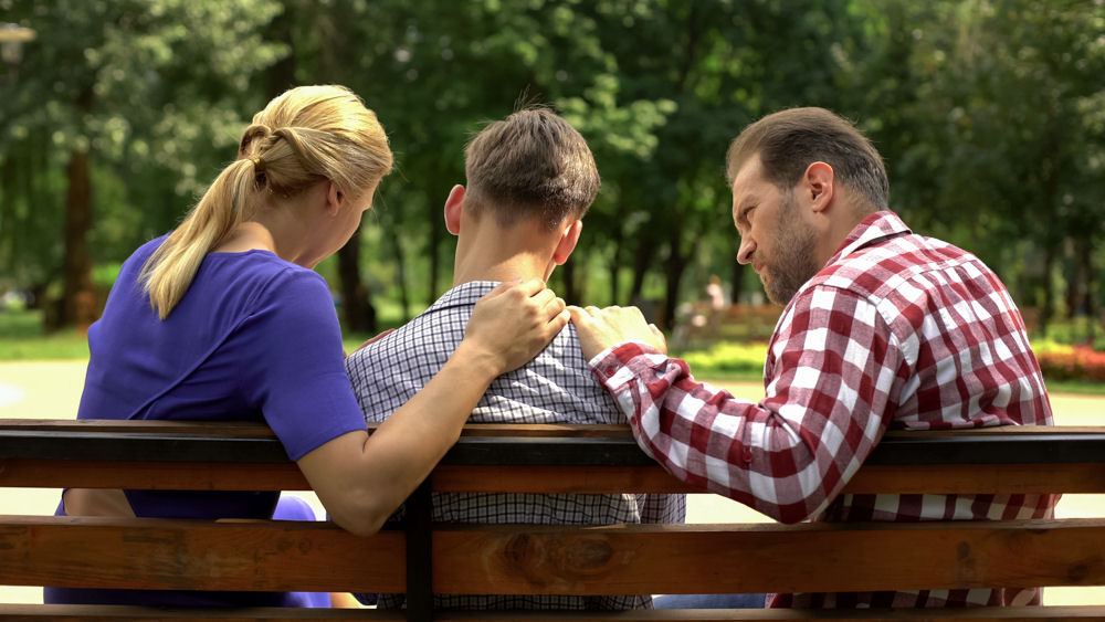 Back view of family having a serious talk with addicted child on park bench