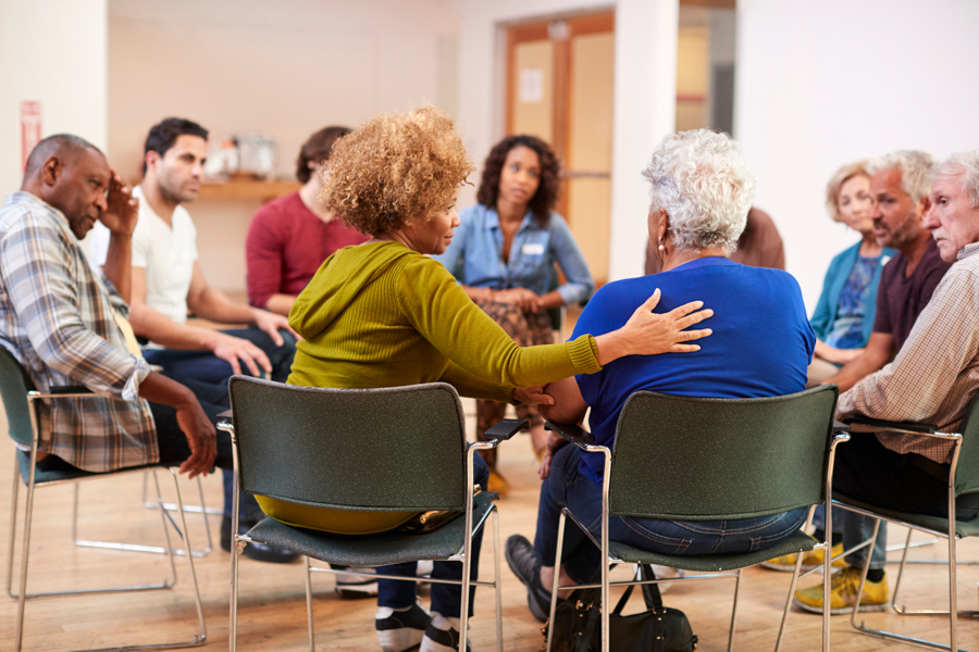 Woman braces shoulder of older woman within group therapy session for opioid addiction support group