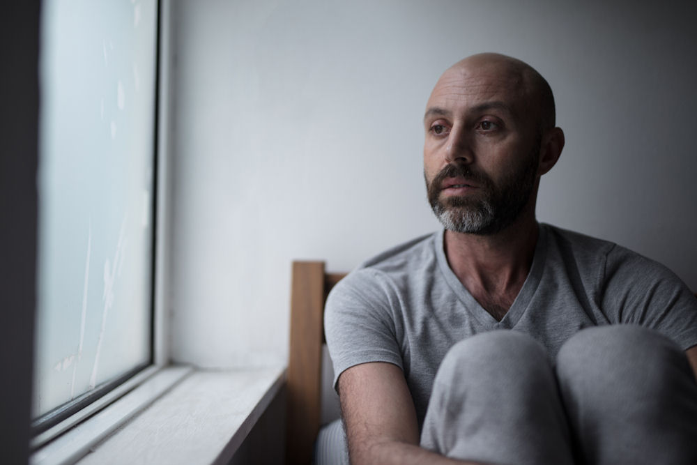 Man detoxing from pink cocaine looking out of rainy window