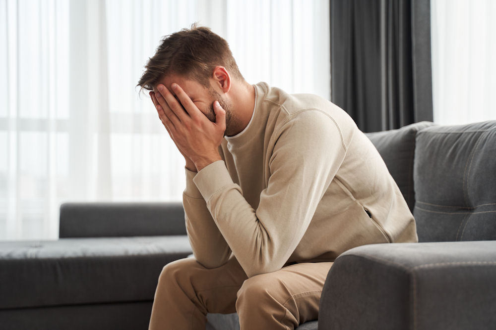 Man sitting on couch holding his face in his hands