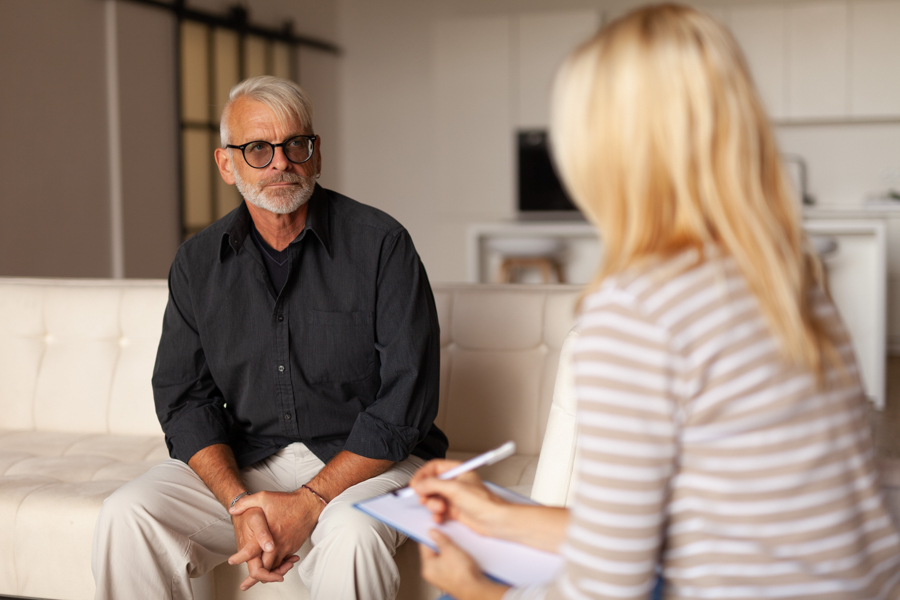 Older man discussing emotional health and mental health with therapist holding clipboard