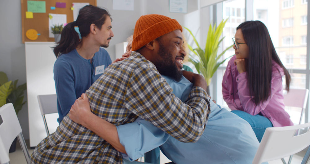 Man embracing another man in support during an addiction support meeting discussing the cycle of addiction