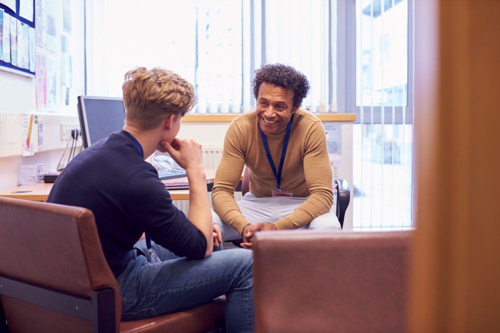 Young counselor smiling while talking to Gen Z man with anxiety