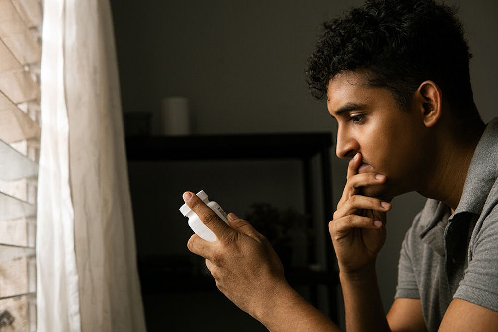 Man looking down at bottle of trazodone in dark bedroom