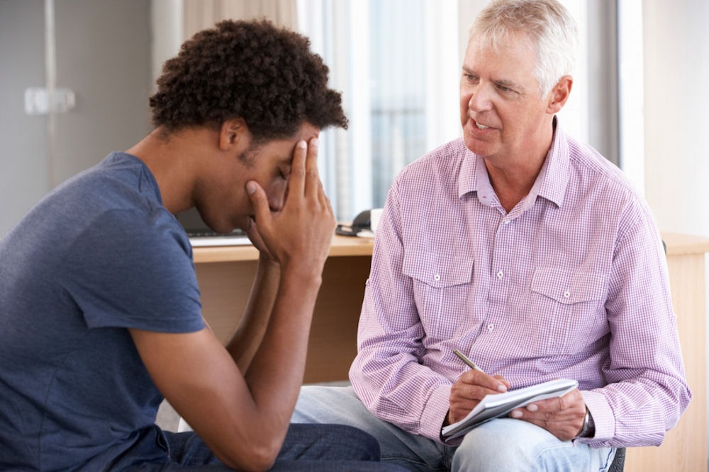 Young man bracing head while talking while therapist takes notes