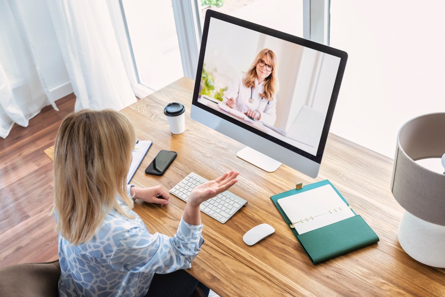 Woman describing symptoms to doctor speaking through telehealth program on desktop computer