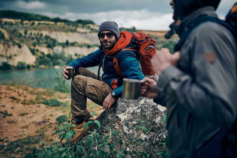 Men sharing coffee while taking a break from climbing up a mountain with foliage