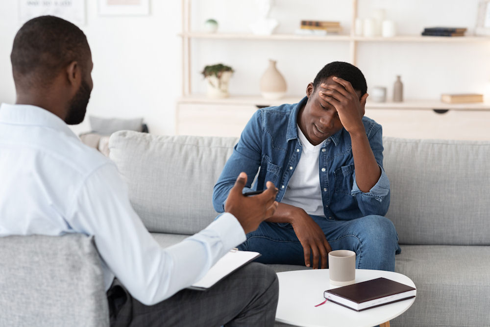 Man with high-functioning anxiety holds head in frustration while talking with therapist