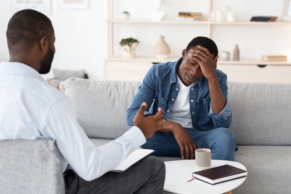 Man with high-functioning anxiety holds head in frustration while talking with therapist
