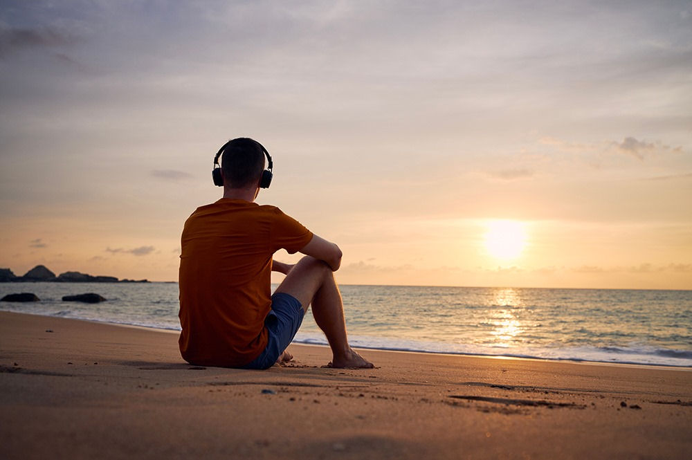 Man with depression wearing can headphones while watching sunset on a beach