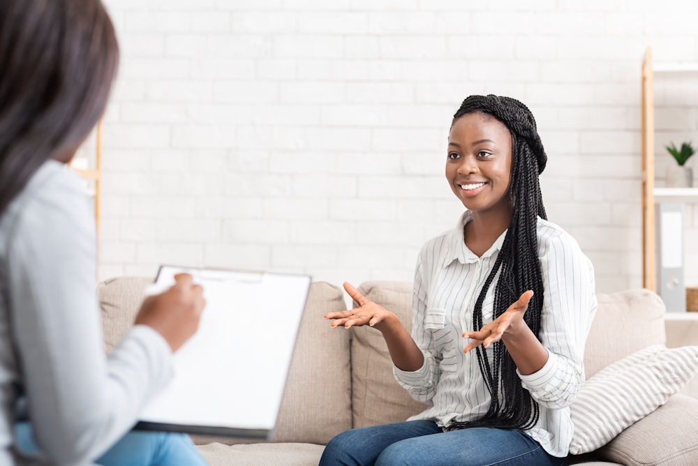 Happy woman holds up hands to gesture during ACT therapy while therapist takes notes.