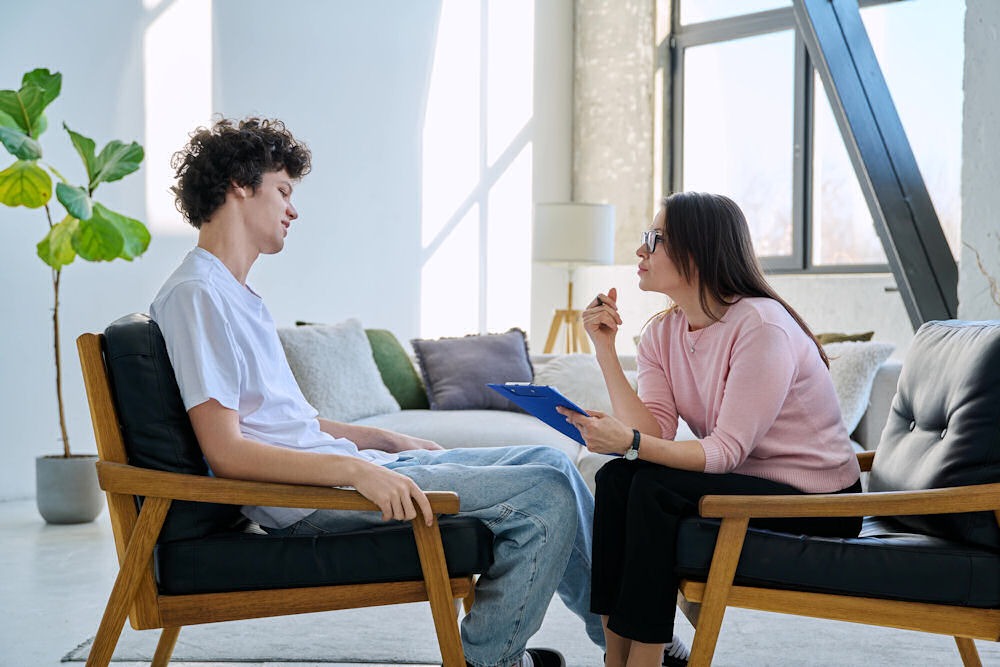 Young man sits back while receiving ACT therapy from woman with glasses.