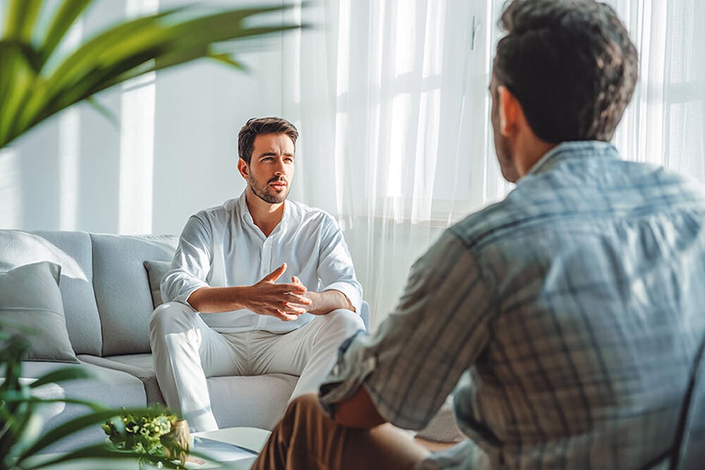 Man receiving therapy from another man in a light-filled office.