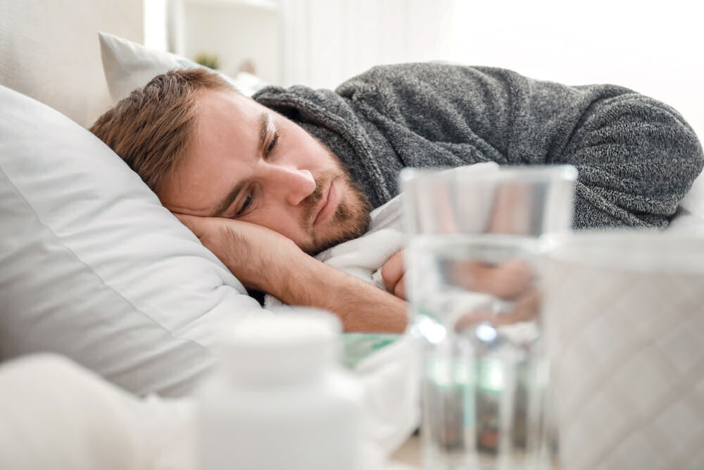 Man sleeping in bed with water and medication on the bedside table.