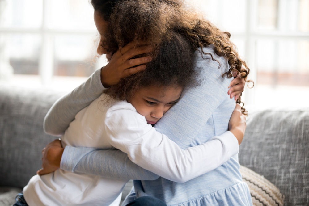 Woman embraces young girl on light-colored couch.