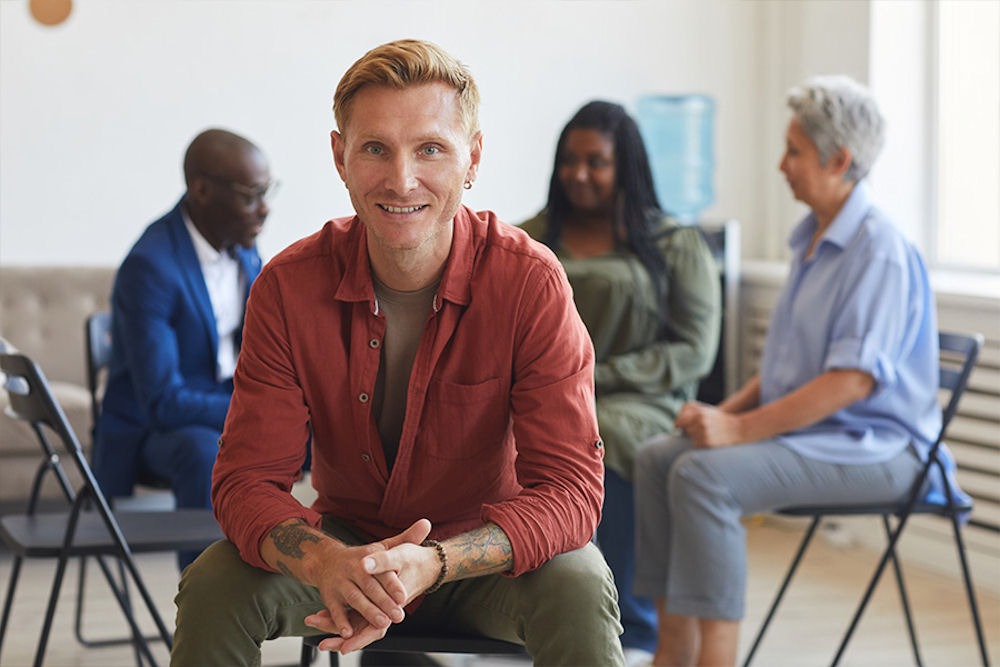 Happy man with tattooed arms looking out from an addiction recovery support group.