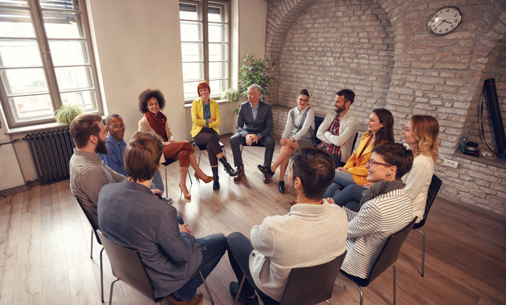 Large addiction group therapy meeting, with everyone sitting on chairs in a loft.
