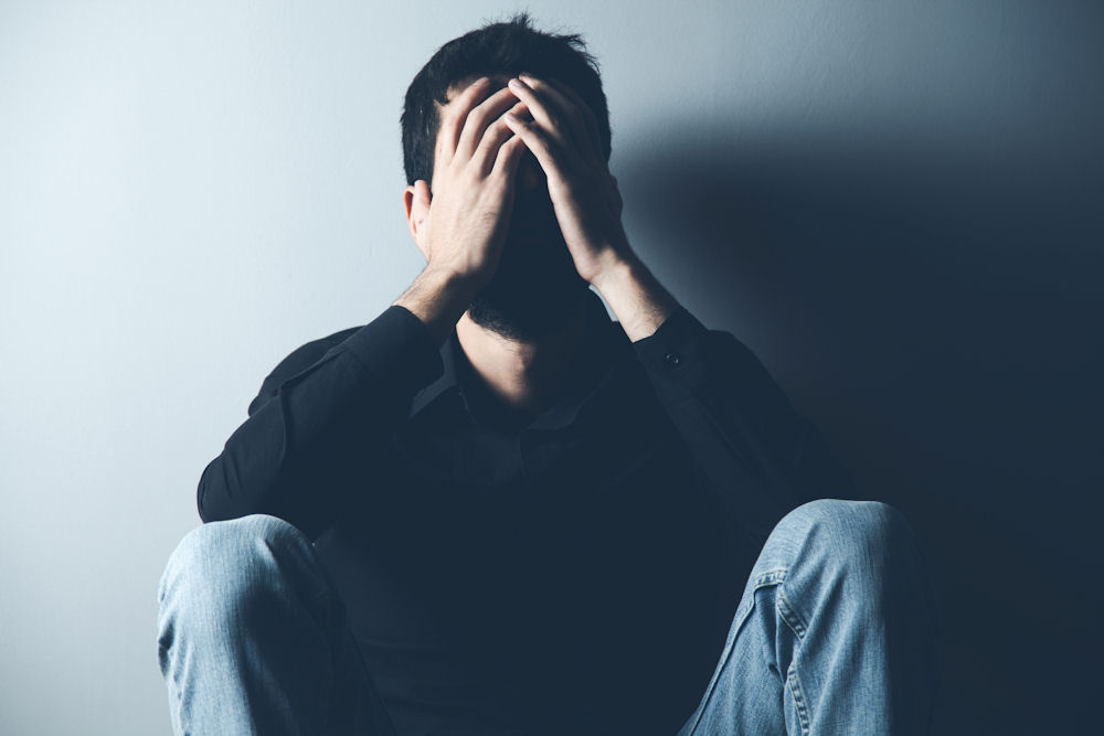 Man with alcohol-induced psychosis holding his head with his face shaded completely.