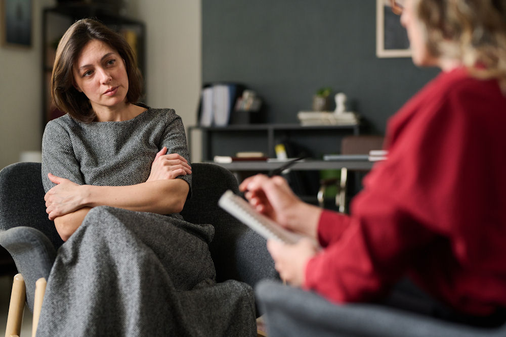 Sad woman with crossed arms listening to therapist with notebook.