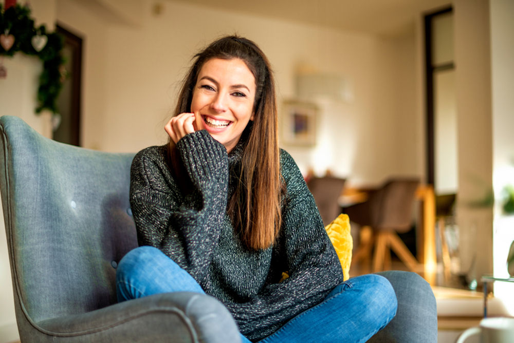 Woman in sweater sitting happily in chair.
