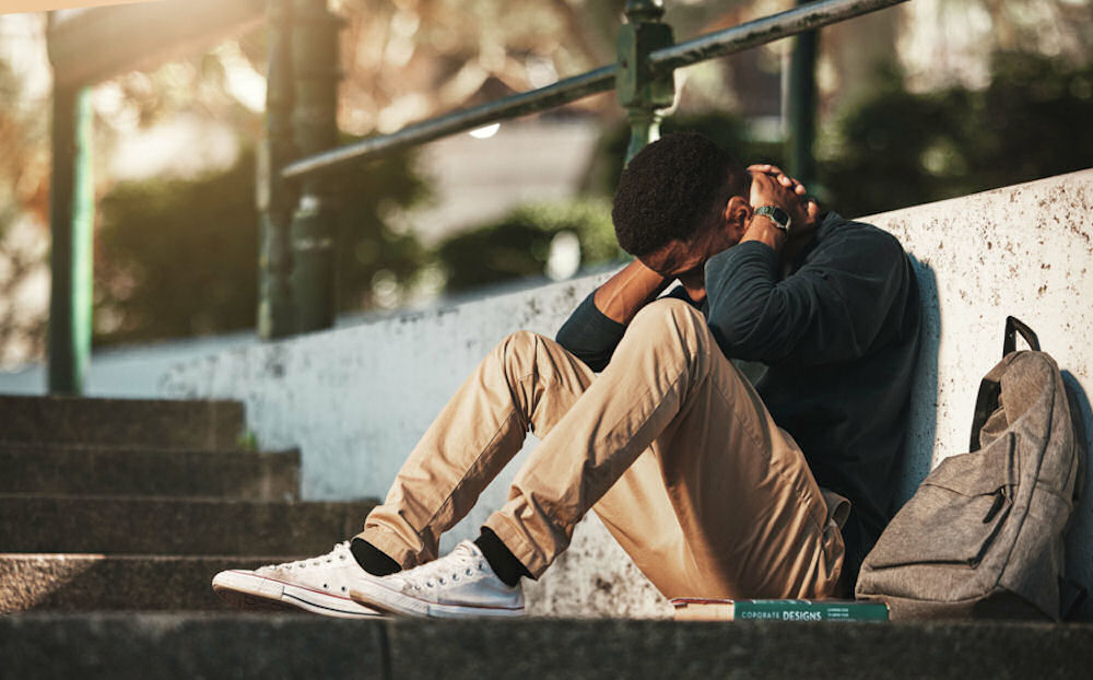 Man with eating disorder sitting on concrete stairs while bracing neck.