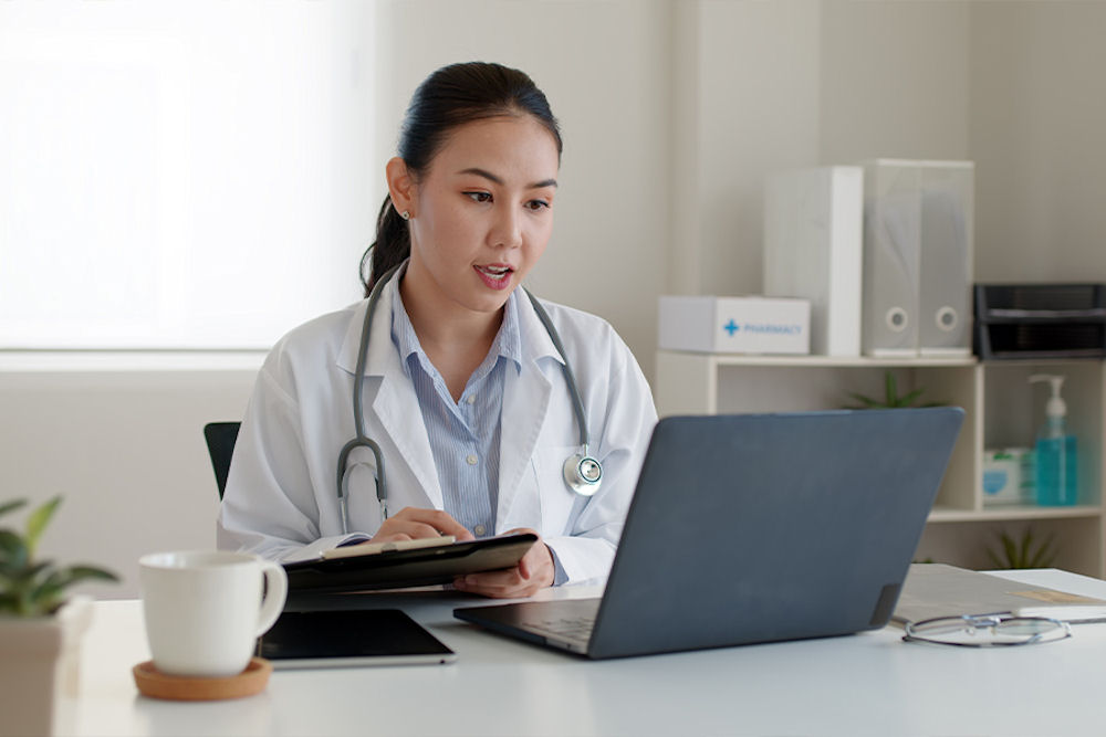Doctor with iPad giving adivce over telehealth treatment on laptop.