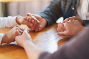 Three people holding hands on a table while disussing anxiety.