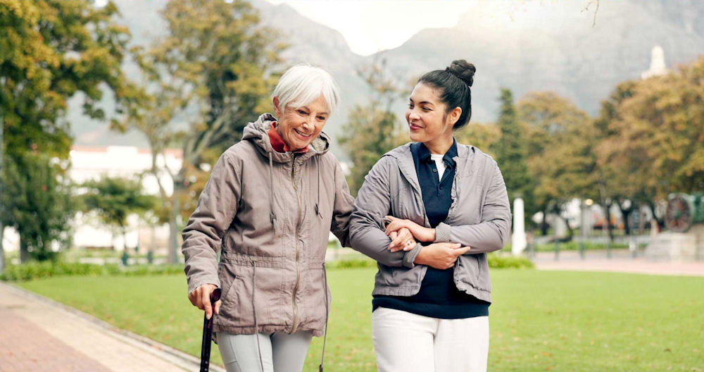 Caretaker walking with older woman while in outdoor park