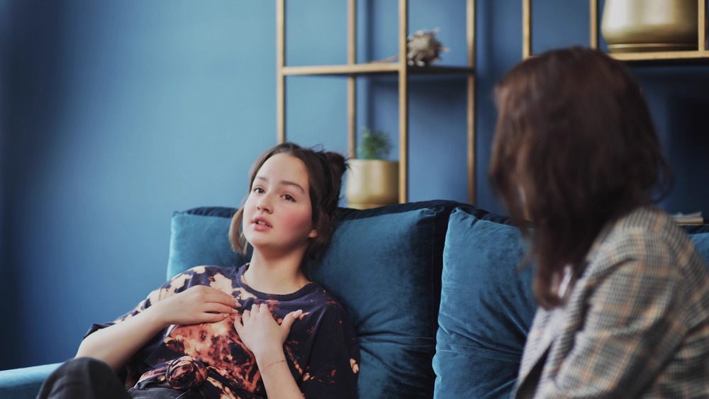 Young woman describes caretaker fatigue with therapist while lying on a blue couch
