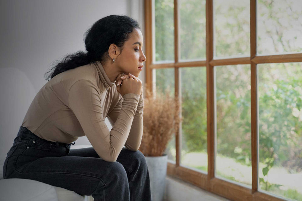 woman gazes out window wondering how to stop chronic lying